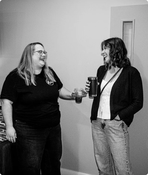 Two women laughing together with a drink in hand